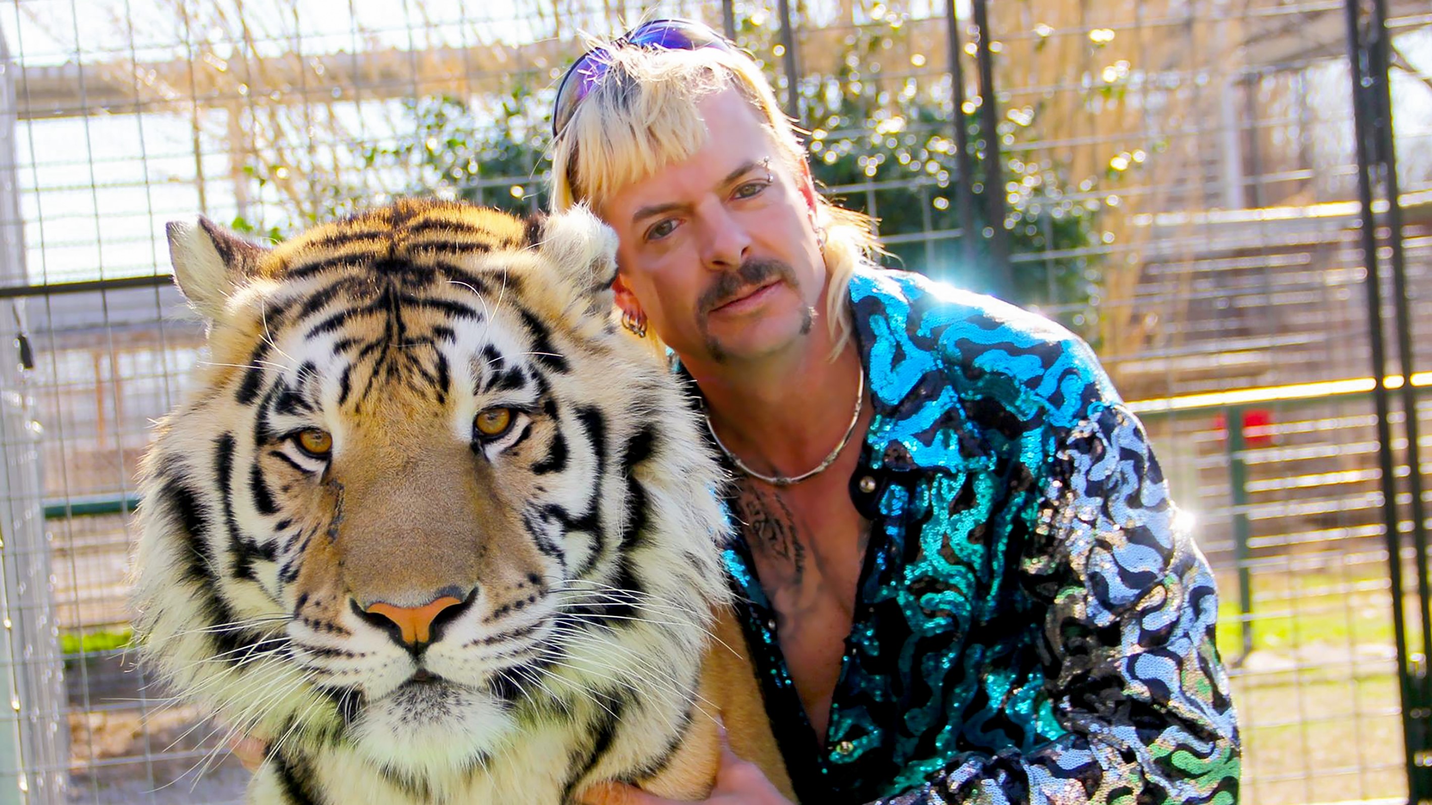 Joe Exotic memakai kemeja bermotif biru berpose dengan seekor harimau.